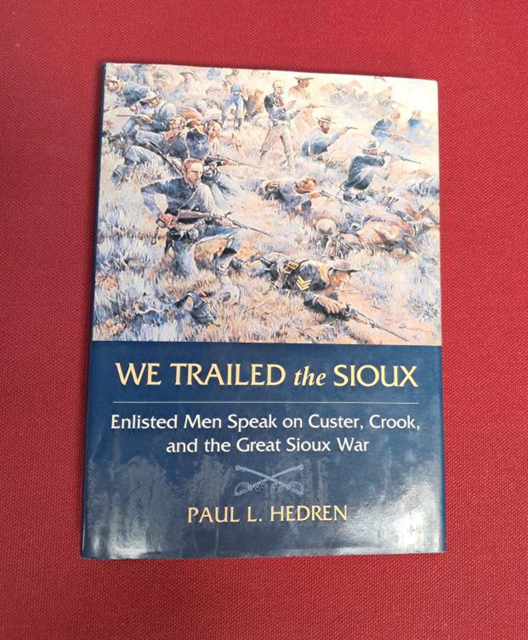 We trailed the Sioux. Top half of the book shows a drawing of soldiers, bottom half is dark blue with yellow/white text. Set on a dark red background